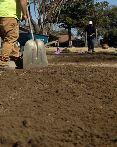 Two people working on landscaping; one holds a shovel, the other stands in the background.